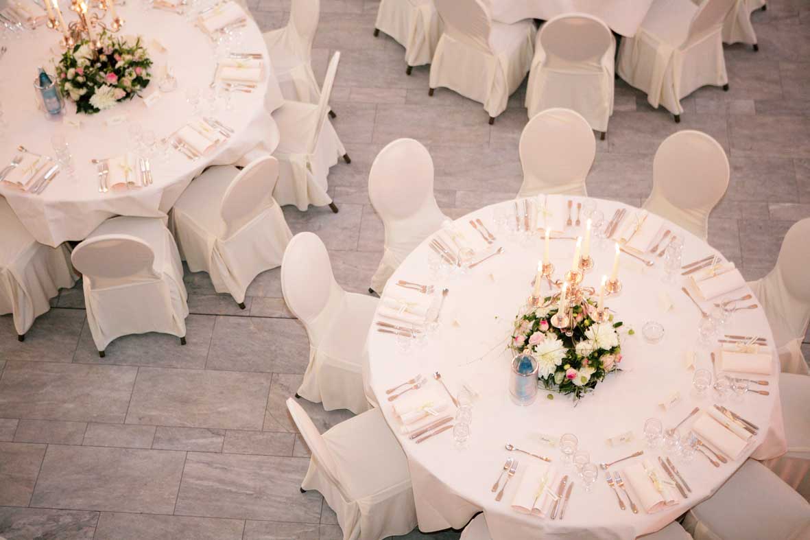 Gedeckte runde Tisch von oben, beige Decken und Stuhlhussen, Blumendekoration in der Mitte, Steinboden